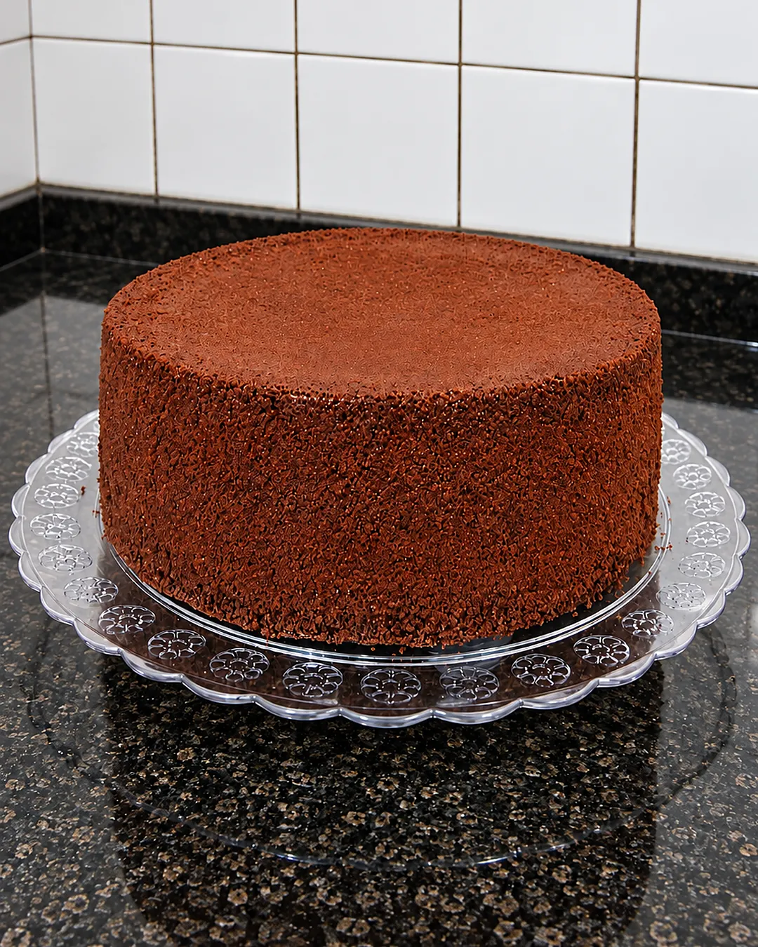 Pão de ló de chocolate alto e fofinho, assado na forma 24 × 10, sobre prato de vidro na cozinha
